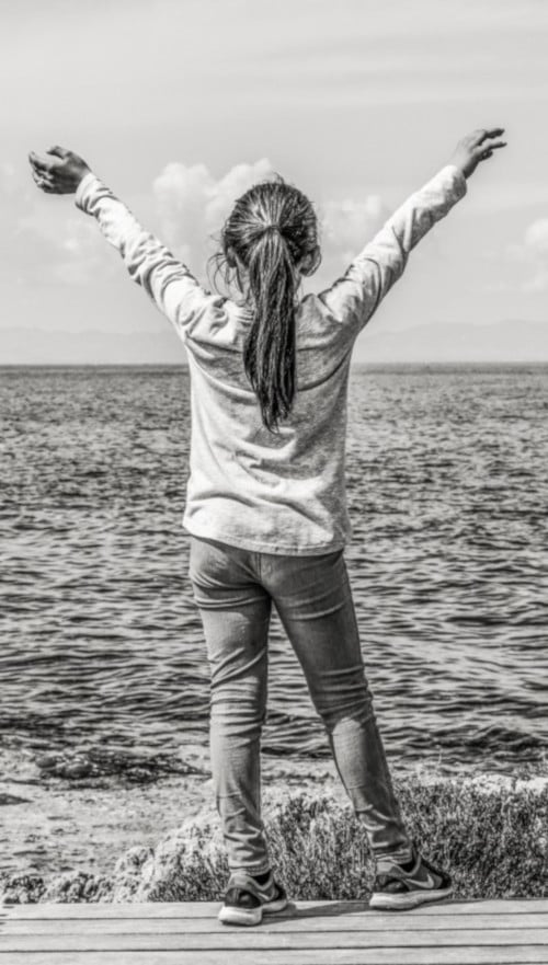 a child standing on a beach, looking at the ocean